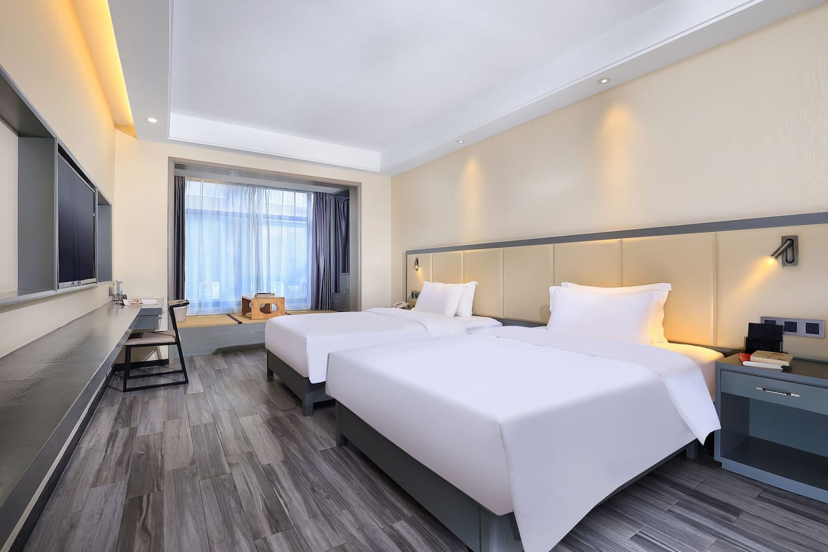 Hotellihuone, jossa on kaksi sänkyä, työpöytä, televisio ja ikkuna, jossa on verhot.