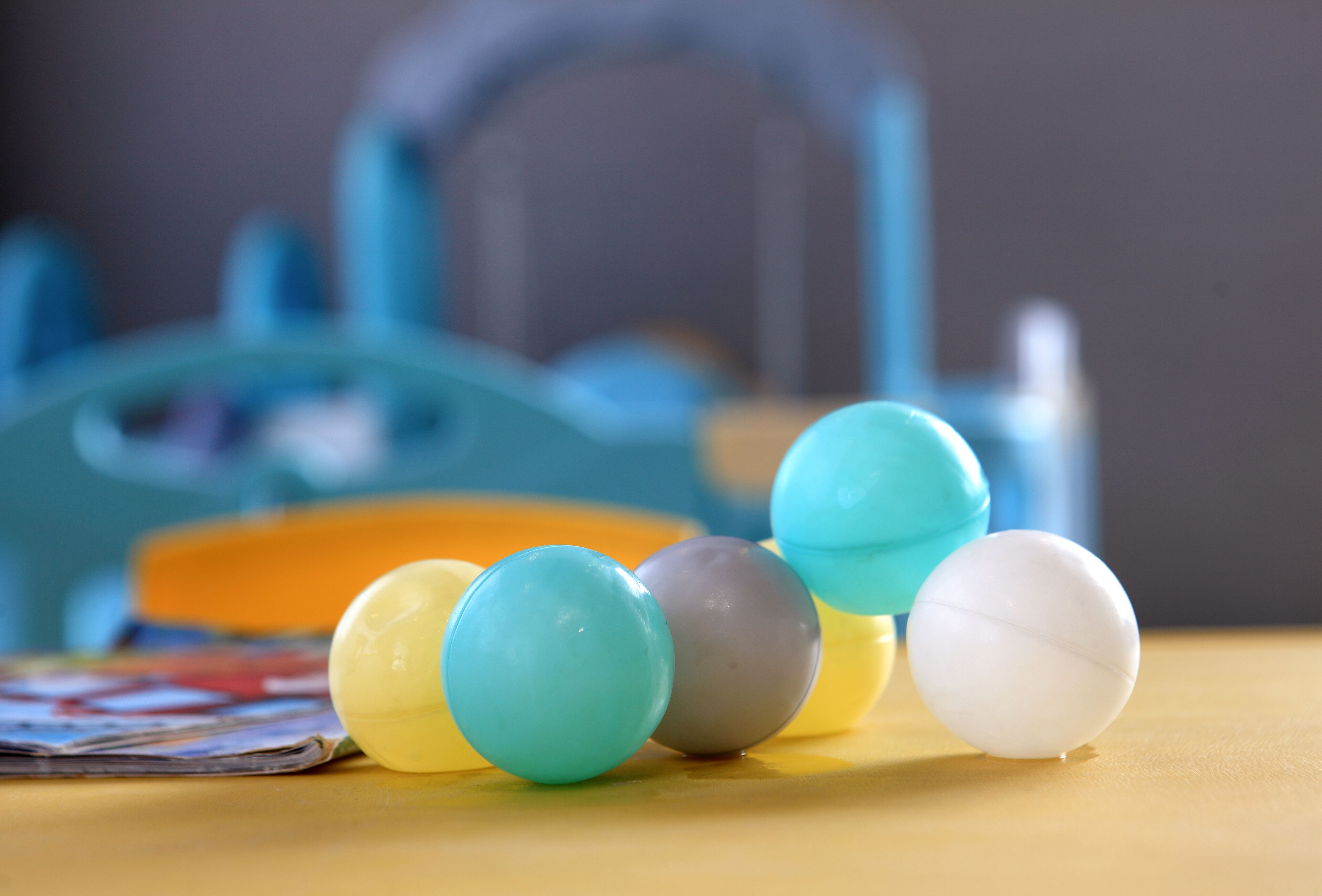 A table with colorful plastic balls and a blue chair in the background.