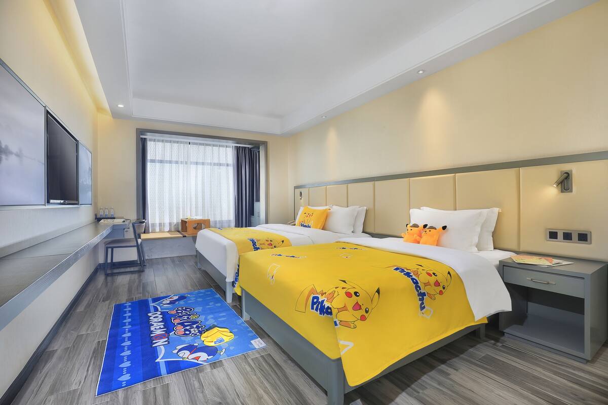 Hotellihuone, jossa on kaksi sänkyä, televisio, ikkuna verhoilla ja pieni pöytä tuolilla.