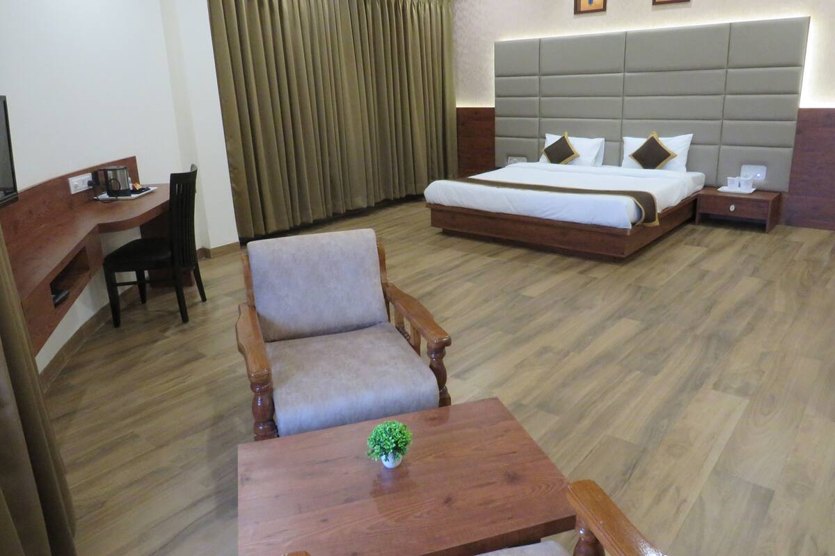 A hotel room with a bed, desk, chair, bedside table, and a small plant.