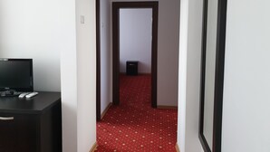 A narrow hallway with a red patterned carpet, a black desk with a television, and a black speaker in the distance. - Hotel Magic City Center (Pitesti)