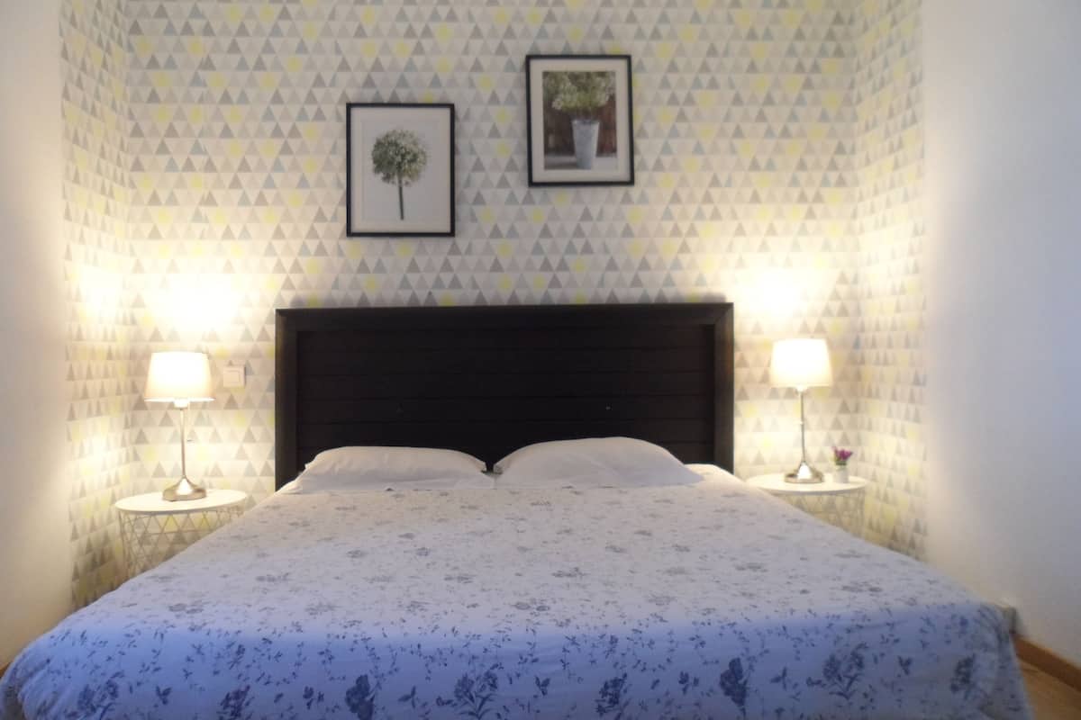 Un lit bien fait, recouvert d’une couvre-lit à motifs floraux, avec deux lampes de chevet et un mur orné d’un motif géométrique.