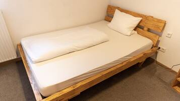A single bed with a wooden frame and white bedding in a room with a carpeted floor and white walls.