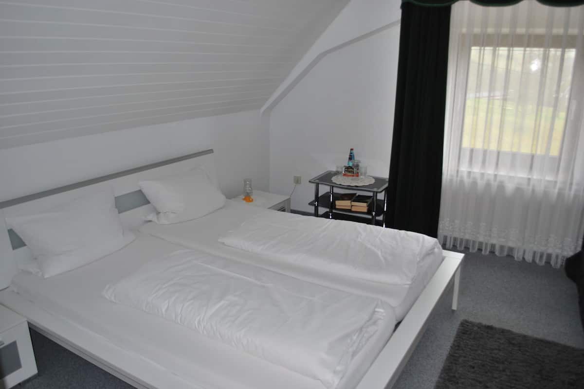 A hotel room with a large bed, a bedside table with a bottle, and a window with curtains.