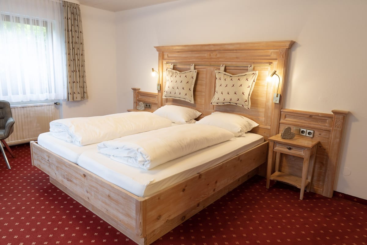 A double bed with a wooden headboard, two bedside tables with lamps, a chair, and a red patterned carpet.
