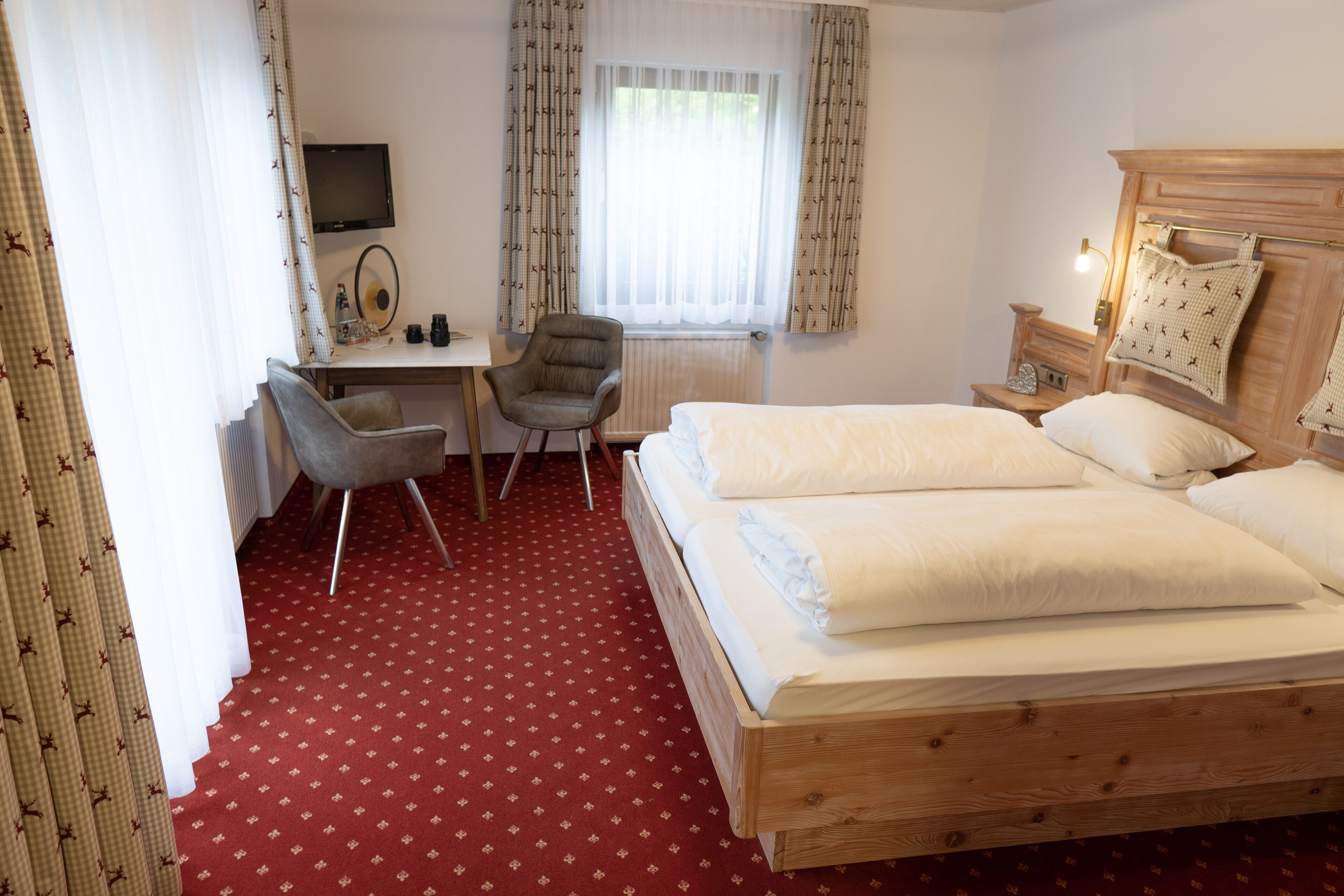 A hotel room with a wooden bed, a desk with a chair, a television, and a window with curtains.
