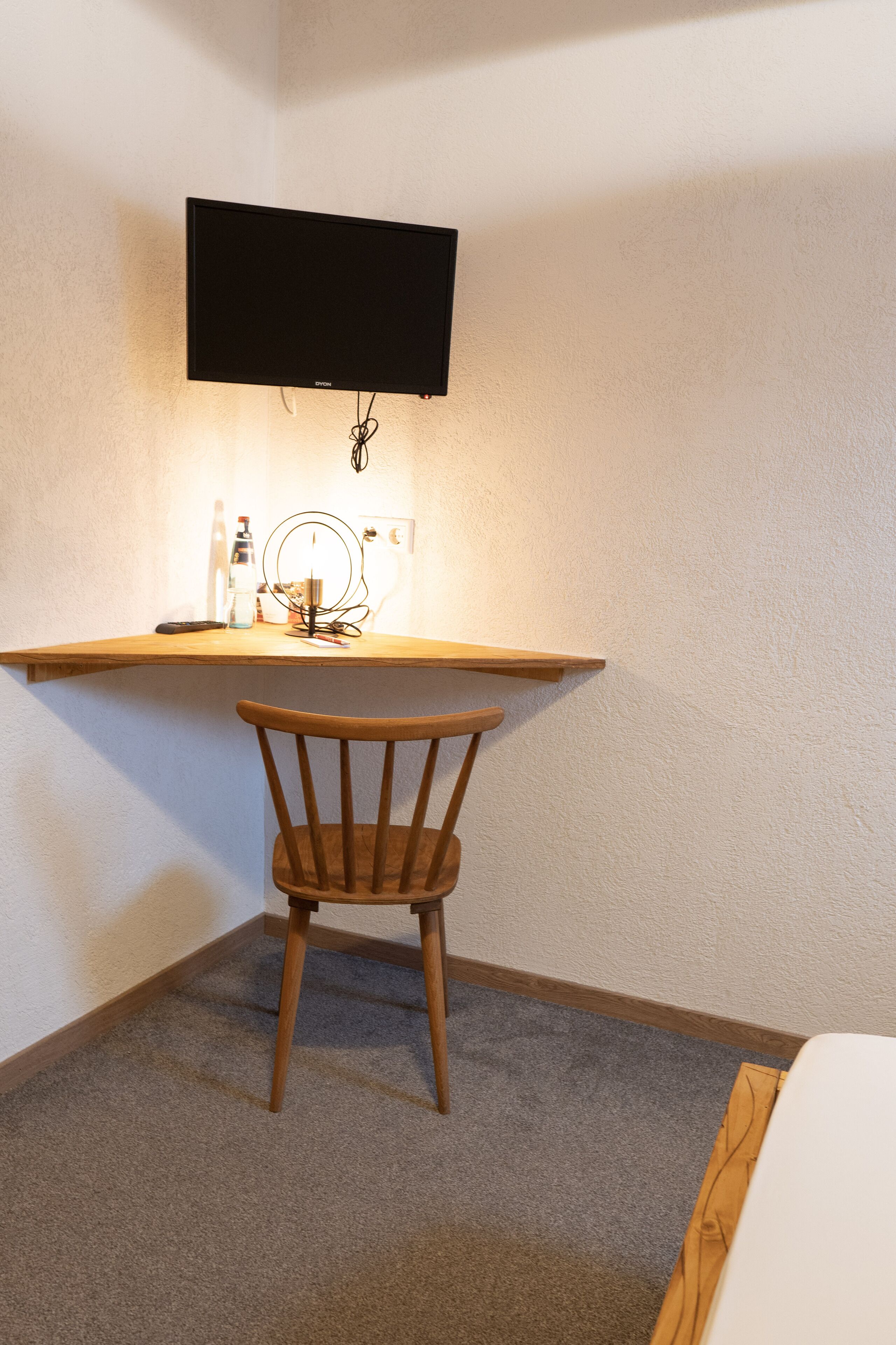 A corner room with a desk, chair, and a mounted flat-screen TV.