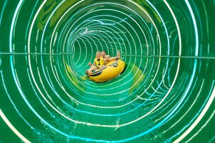Un tobogán acuático con una persona y un niño en un flotador amarillo.