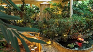 An indoor garden with a stone fountain, seating area, and a wooden structure.
