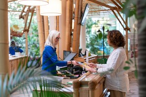 A person at a counter in a bamboo-themed indoor setting with a digital screen and a cash register. - Hotel Hochsauerland by Center Parcs (Medebach)