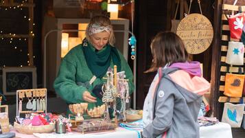 A person at a market stall with various items on display, including hanging decorations and a sign with text.