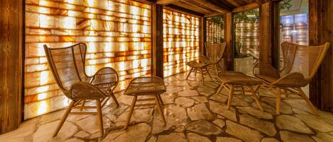 A covered outdoor seating area with stone flooring and wooden furniture.