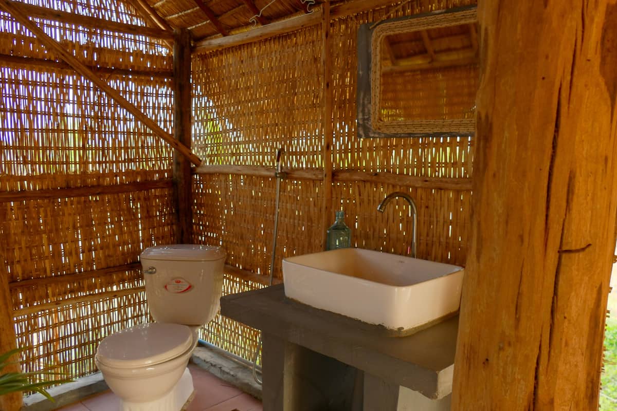 A rustic bathroom with a bamboo wall, a toilet, and a sink.