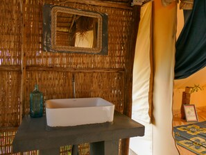 Een badkamer met een wand van geweven bamboe, een witte wastafel, een spiegel en een handdoek aan de rechterkant.