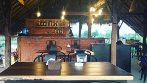 An outdoor dining area with brick walls, wooden tables, and black chairs. - Salt Field Glamping (Kampot)
