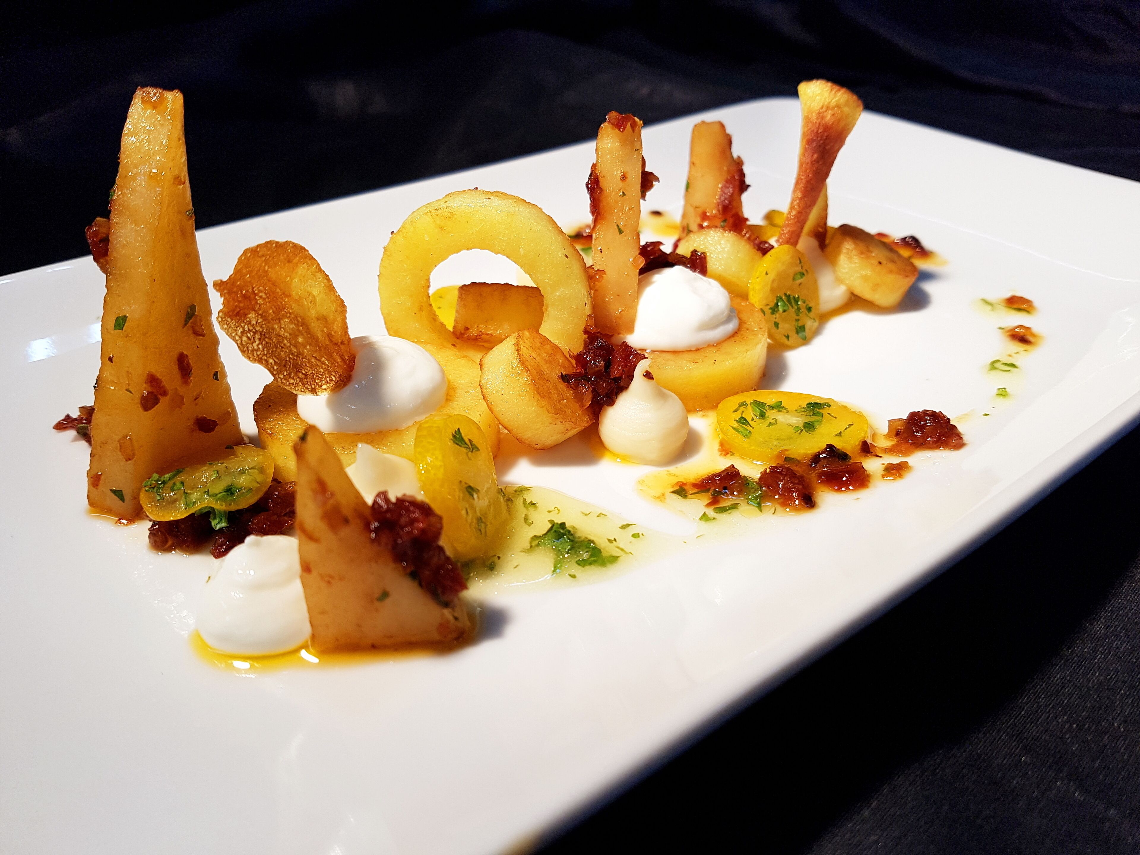 A white plate with a variety of food items including potatoes, a dollop of cream, and some garnishes.