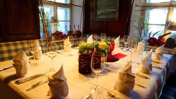 A dining table set with white tablecloths, neatly arranged cutlery, and red candle holders.