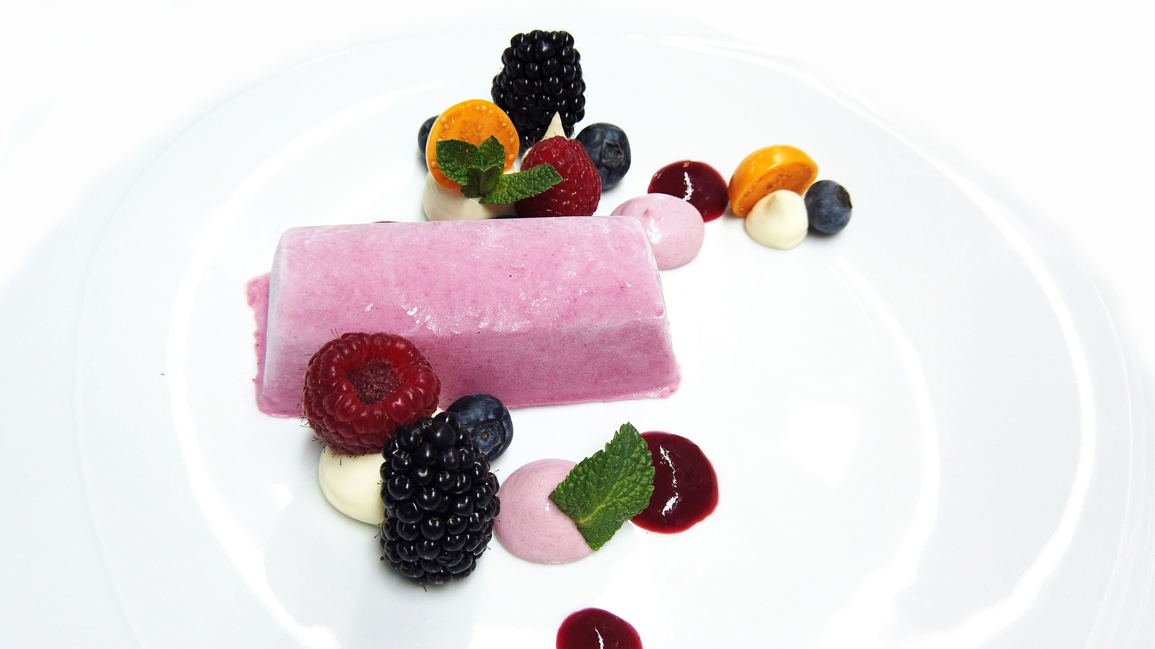 A dessert with various berries and a pink ice cream bar on a white plate.