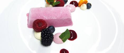 A dessert with various berries and a pink ice cream bar on a white plate.