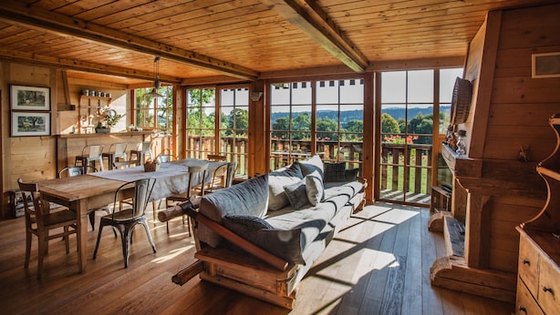 A wooden cabin interior with a dining area, sofa, and large windows offering a view of the outdoors. - Maison d'hôtes Le Pré Oudot (Fournets-Luisans)
