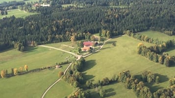 Vue aérienne d’une propriété rurale comprenant un vaste champ ouvert, un bâtiment à toit rouge et des zones boisées environnantes.