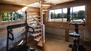 A gym with a treadmill, a stationary bike, and a wooden staircase. - Maison d'hôtes Le Pré Oudot (Fournets-Luisans)