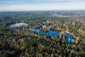 An aerial view of a resort with a large building, a lake, and surrounding forest. - Hotel Bispinger Heide by Center Parcs (Bispingen)