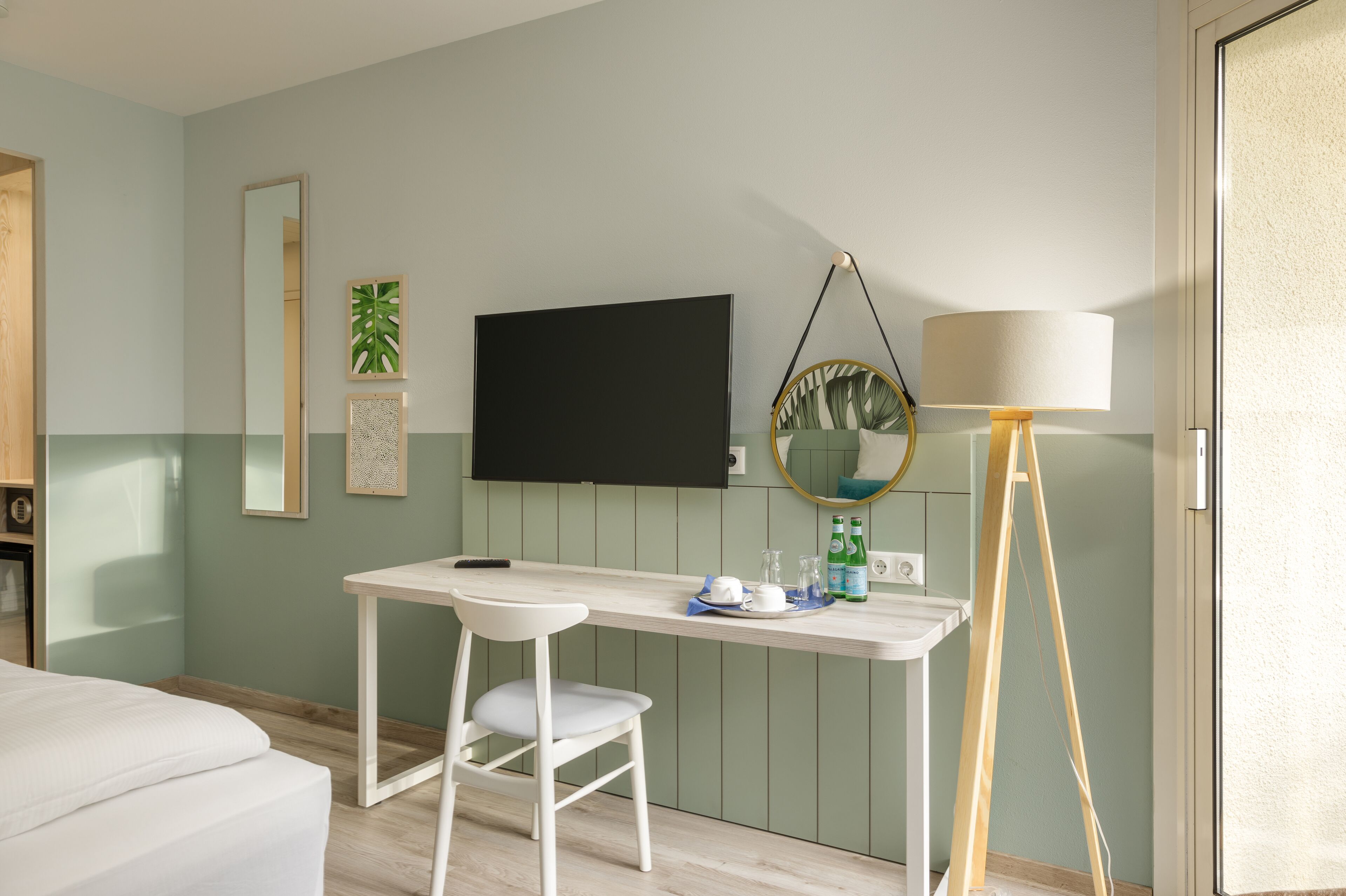 A room with a bed, a desk with a chair, a TV, a mirror, and a lamp.
