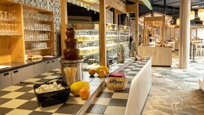 L’intérieur d’un café avec un sol à carreaux, des étagères en bois où sont disposés des verres, une fontaine à chocolat et un présentoir de fruits.