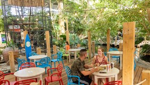 Un espace de restauration en plein air avec des tables et des chaises en bois, entouré de verdure et délimité par des barrières en corde.