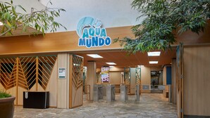 L’entrée d’un hôtel, avec un sol carrelé en pierre, un comptoir d’accueil en bois et une enseigne indiquant « AQUA MUNDO ».