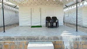 Un espace sous une tente comprenant une scène, deux chaises et un tapis vert.