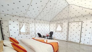 Une pièce aménagée avec une tente, un lit, deux chaises et une petite table.