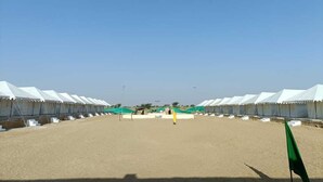Une rangée de tentes blanches, séparées par un sol sablonneux, sous un ciel bleu dégagé.