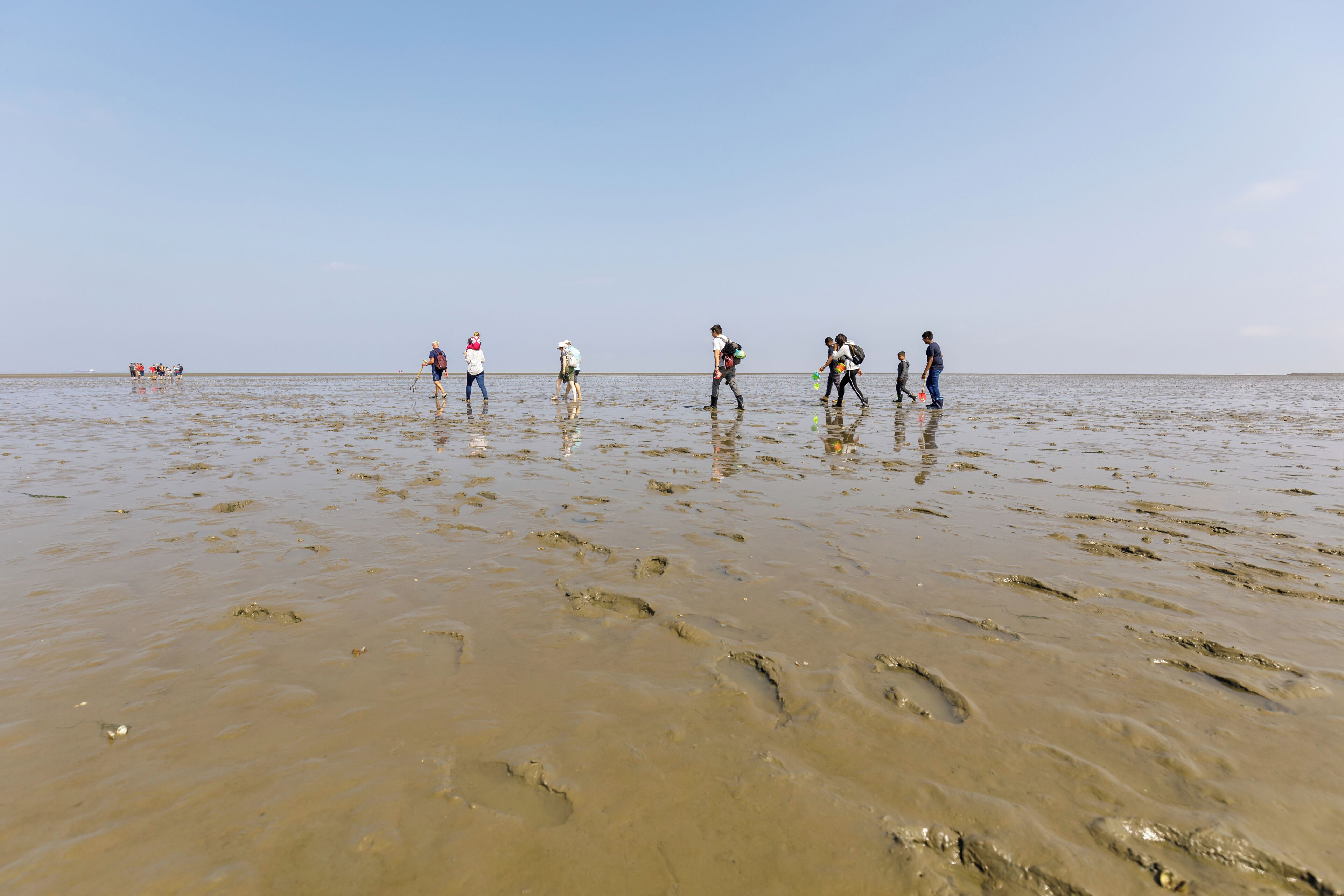 A beach with people walking and standing in shallow water.