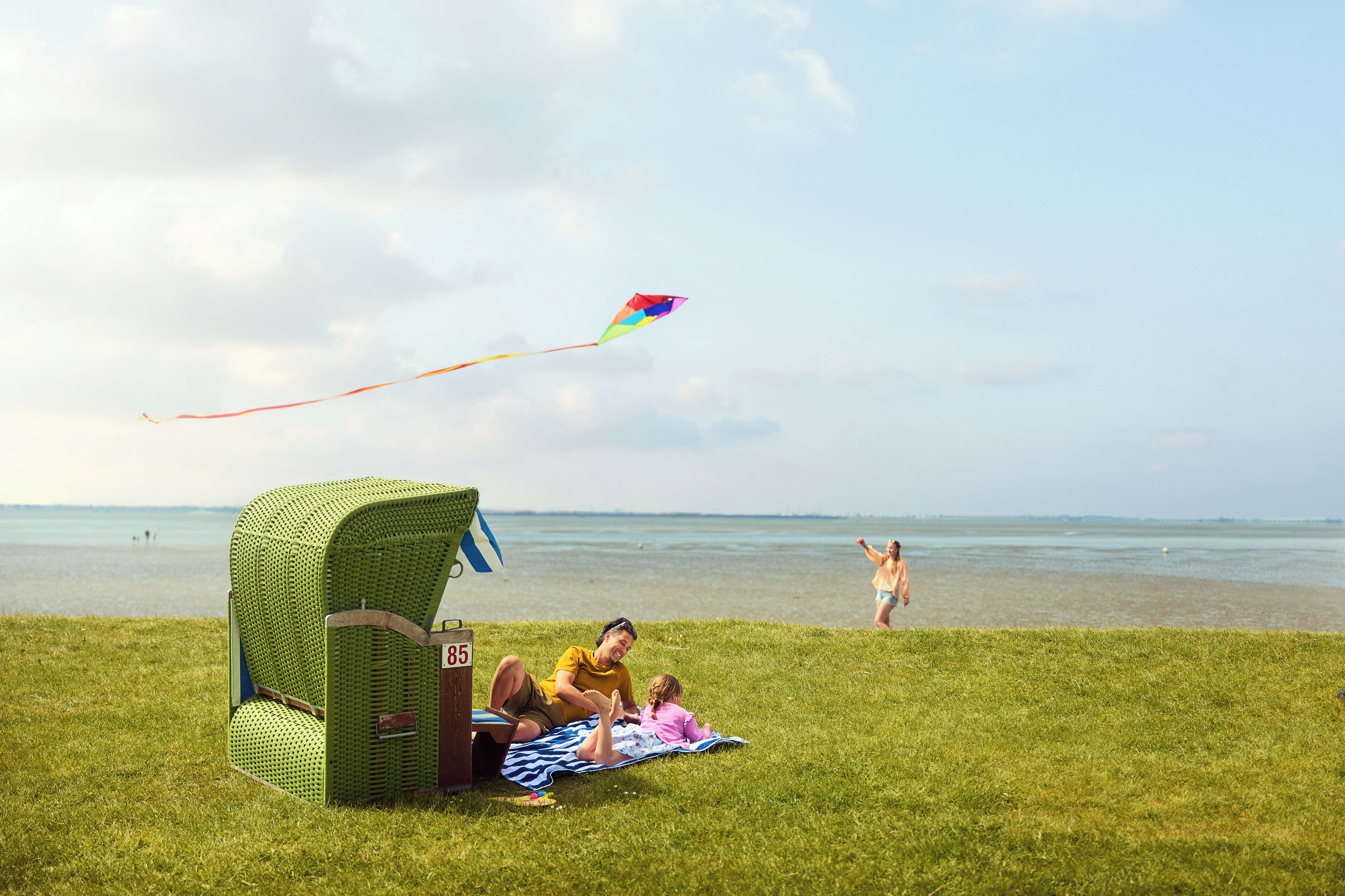 A grassy area with a green playhouse, a beach in the background, and a kite flying.