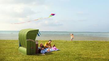 Zona verde con una casita de juegos, una playa al fondo y una cometa volando.