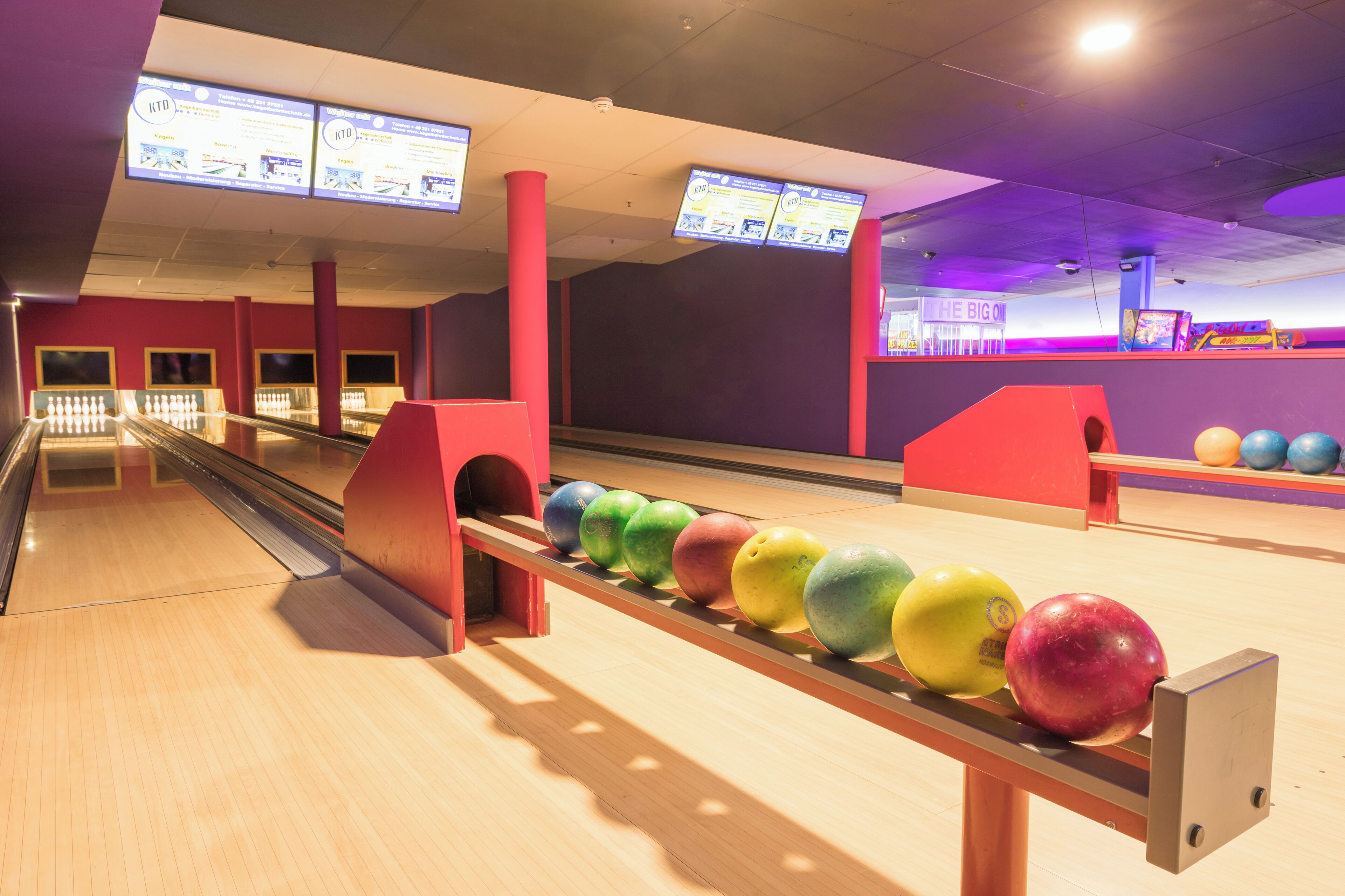 A bowling alley with multiple lanes, a bowling ball return system, and overhead digital scoreboards.