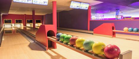 Bolera con múltiples pistas, sistema de devolución automática de pelotas y marcadores electrónicos sobre la pista.