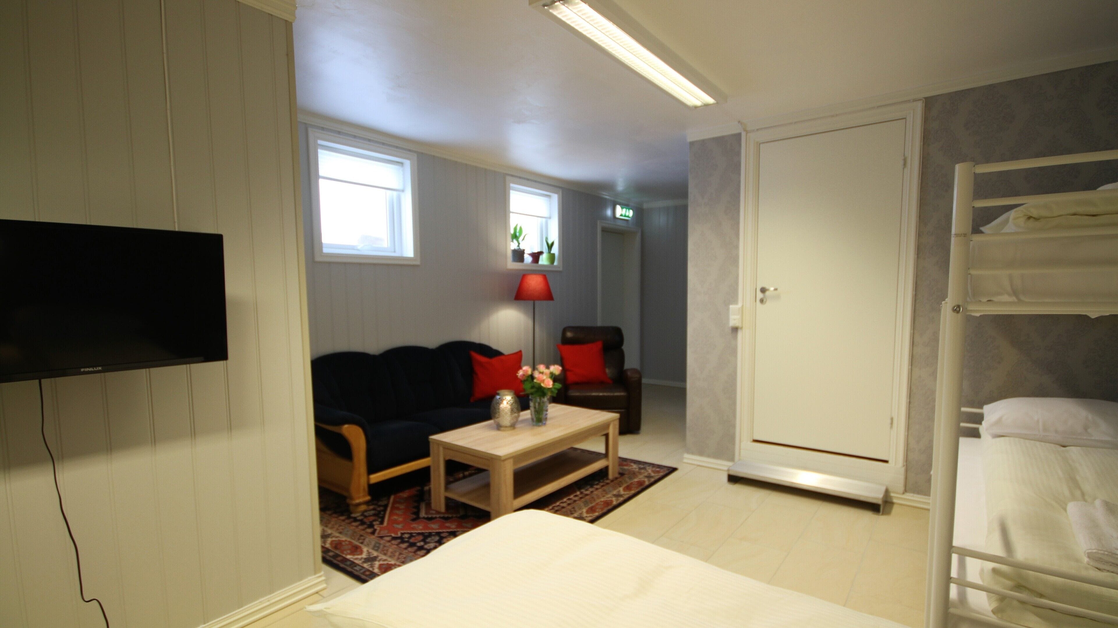 A compact hotel room with a bed, a sofa, a small table with a vase, a TV, and a wardrobe.
