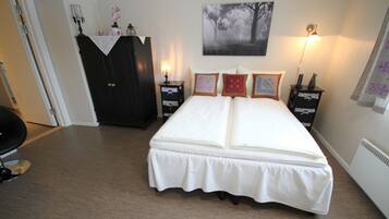 A bedroom with a large bed, a dark wooden wardrobe, bedside lamps, and a wall-mounted picture.