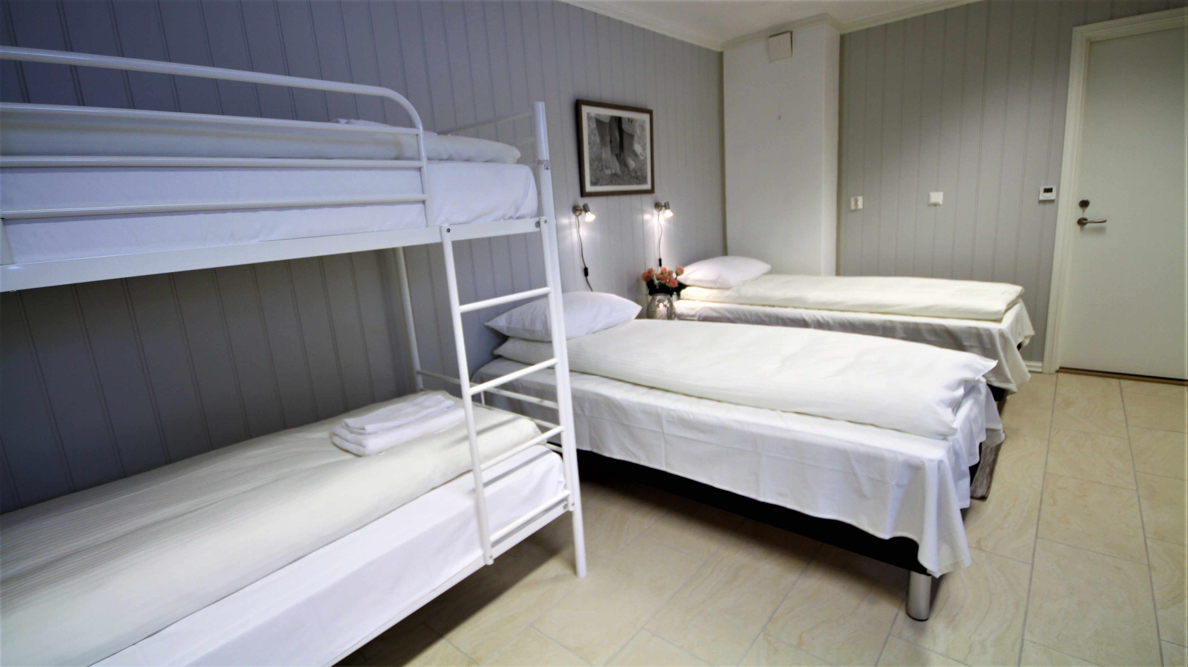Una habitación con literas, una mesita de noche con lámpara y una puerta.