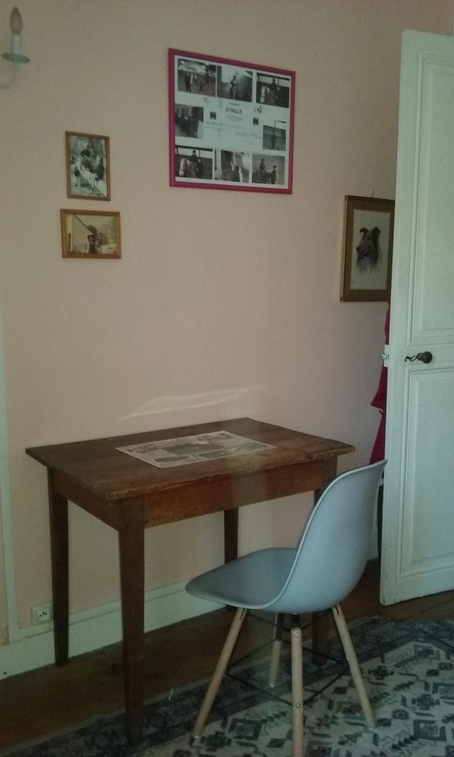 A room with a wooden table, a single chair, and a door. There are framed pictures on the wall.