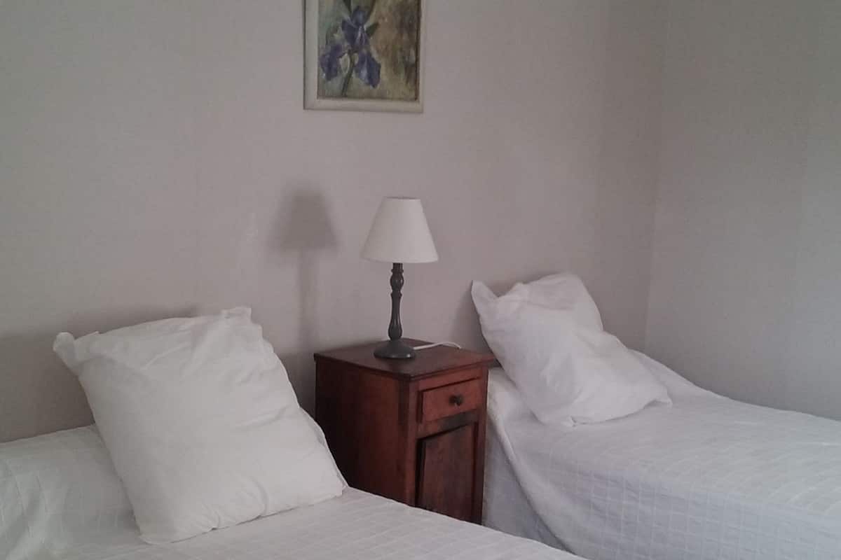 A hotel room with two single beds, a nightstand with a lamp, and a painting on the wall.