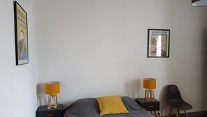 Un dormitorio con una cama, dos mesitas de noche con lámparas, una silla y dos cuadros en la pared.