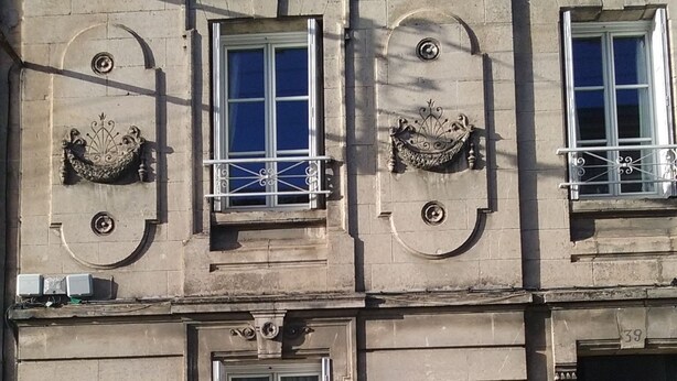 Un edificio con tres ventanas, cada una con un balcón decorativo. Se observa una puerta a la derecha y un ventanal pequeño a la izquierda.