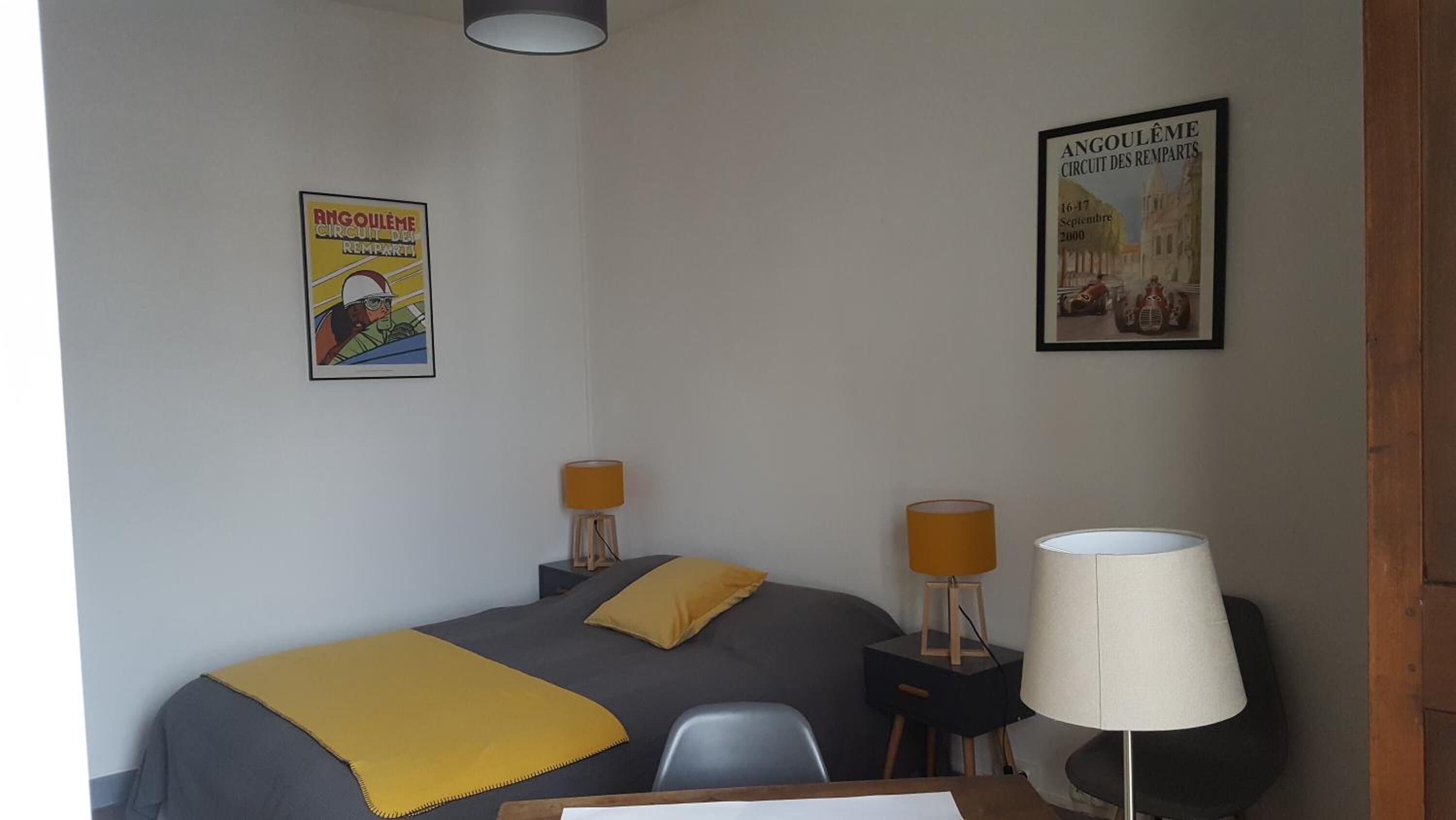 Una habitación de hotel con una cama, dos mesitas de noche con lámparas, un escritorio y dos carteles en la pared.