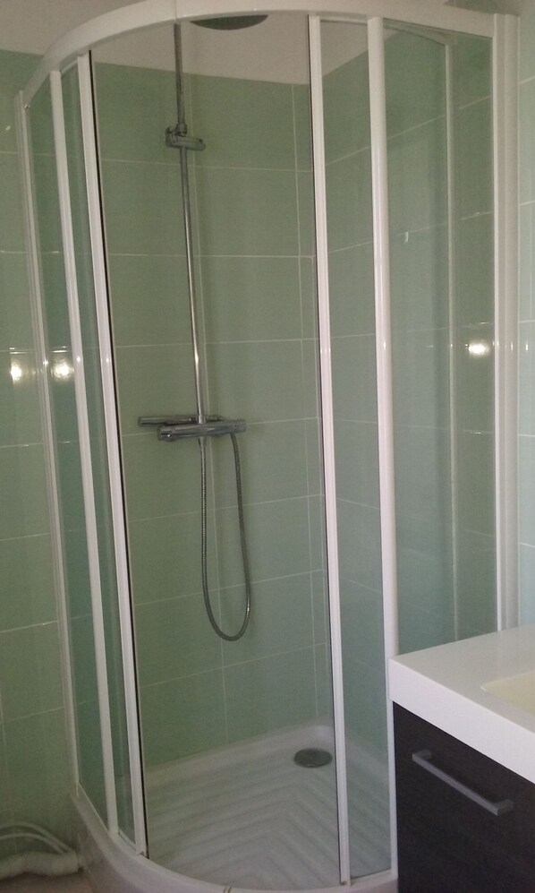Ducha de esquina con mampara de vidrio, lavamanos blanco y mueble de color oscuro.