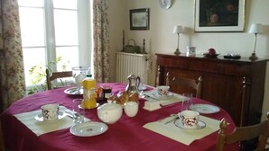 Mesa lista para comer con platos, tazas y una jarrón, rodeada de sillas.