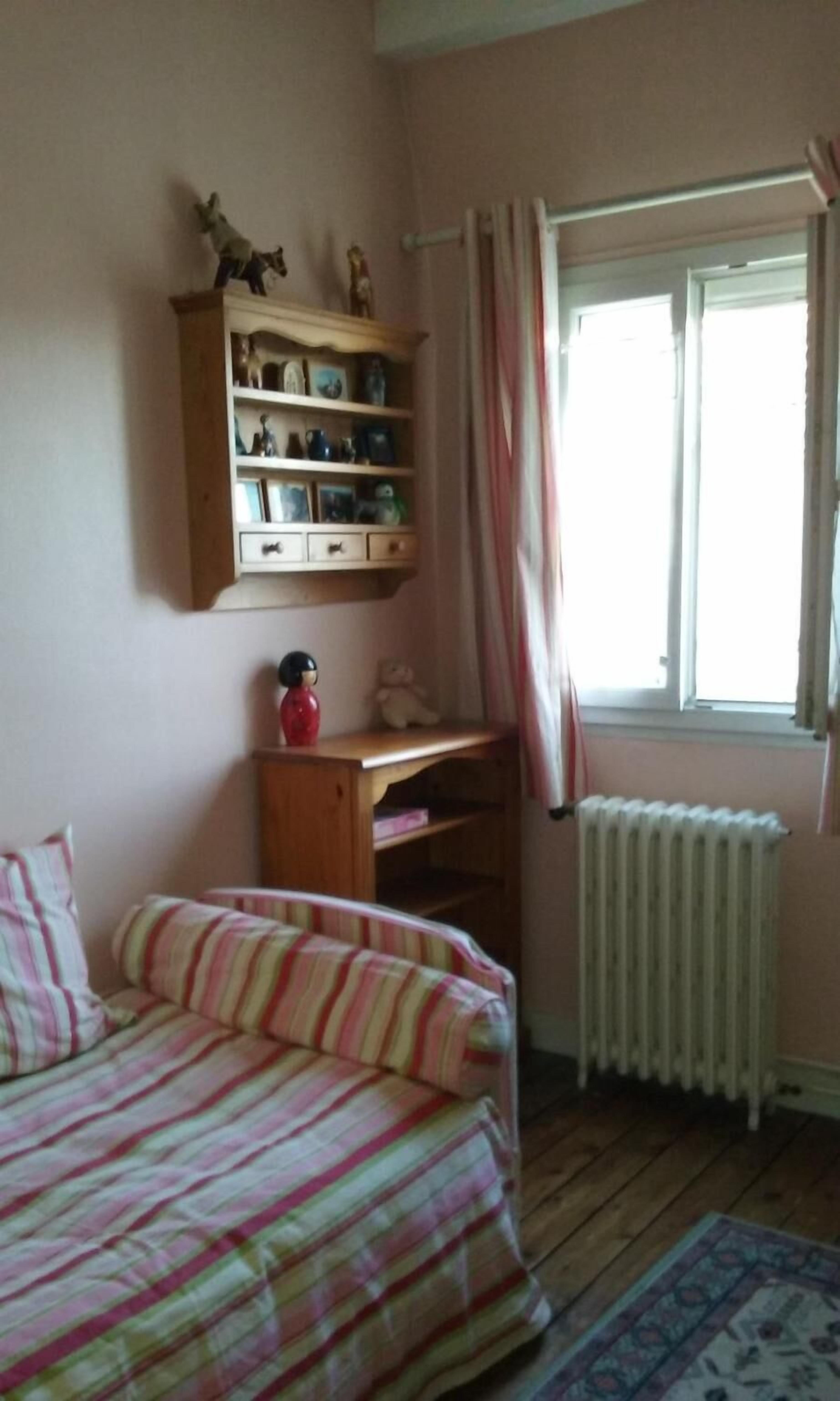 Un dormitorio con una cama, un escritorio de madera, un radiador y una ventana con cortinas.